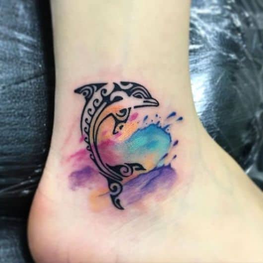 Tatuagem de um golfinho feito com traços tribais saltando de uma água feita em tons de aquarela. 