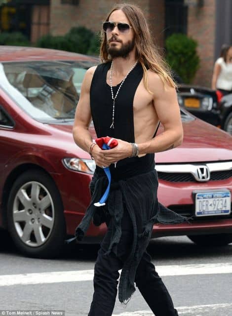 O ator Jared Leto caminhando na rua vestindo uma regata cavada masculina preta sem estampa com um colar e uma blusa amarrada na cintura. 