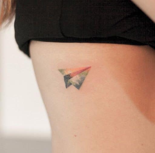 Tatuagem pequena de um avião de papel feito na costela colorido com cores quentes. 