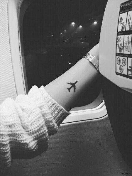 Tatuagem delicada do contorno de um avião preenchido de preto feita no antebraço de uma pessoa que está dentro de um avião. 