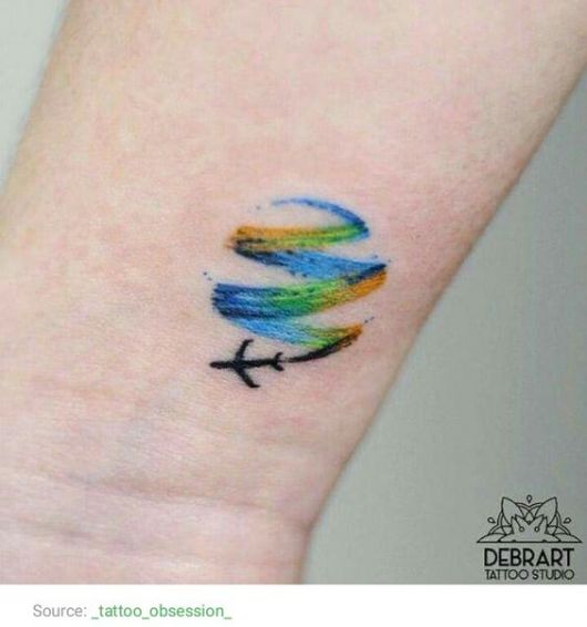 Tatuagem delicada no pulso de um avião voando enquanto deixa um rastro que é feito com aquarela. 