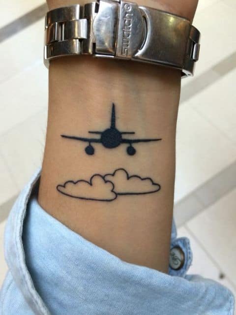 tatuagem da silhueta de um avião sobrevoando os céus com duas nuvens abaixo dele. 