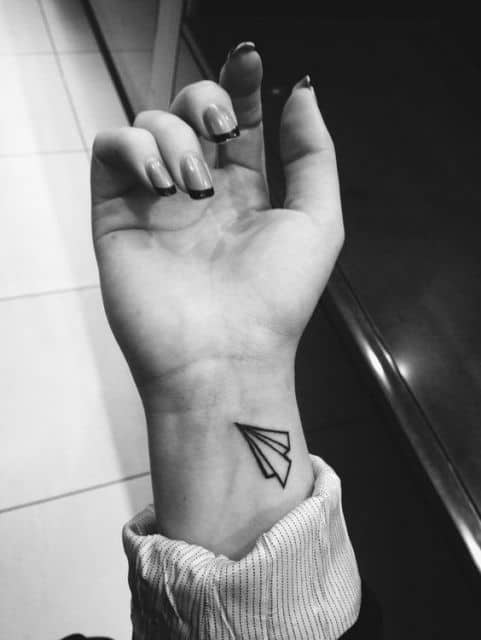 Tatuagem simples de um avião de papel feito no pulso. 