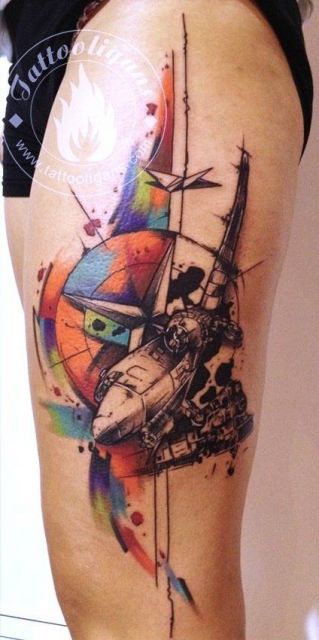 Tatuagem de aquarela feita na coxa de uma pessoa com um avião de guerra em frente a uma bússola grande redonda. 