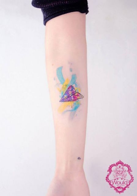 Tatuagem de um avião de papel simples feita no antebraço com detalhes também coloridos ao seu redor. 