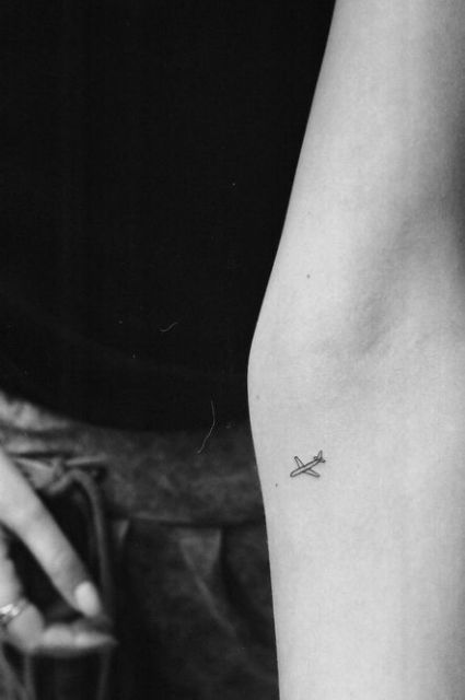 Tatuagem muito pequena de um avião simples feito somente a partir de linhas no antebraço.
