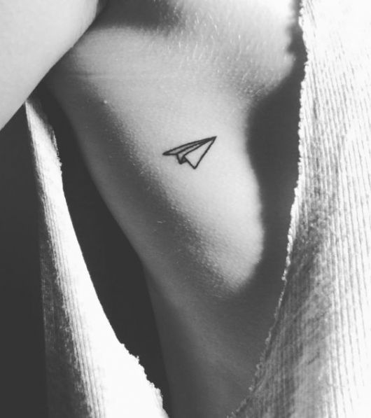 Tatuagem de um avião de papel delicada feita nas costelas de uma mulher. 