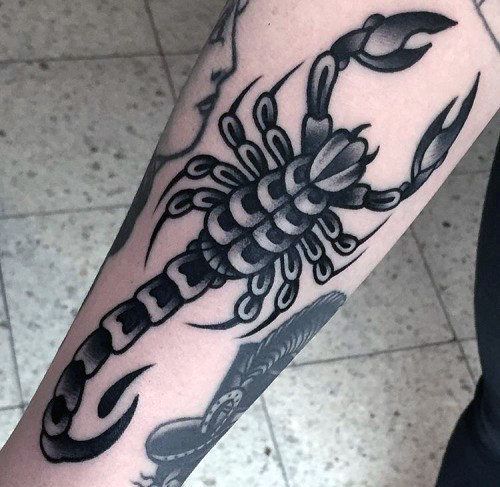 Tatuagem de um escorpião visto de cima feita toda em tons de cinza próxima a outras tattoos com estética semelhante. 