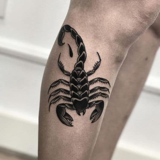 Tatuagem de escorpião feita na perna em tons escuros posicionada entre a lateral do joelho e da canela. 
