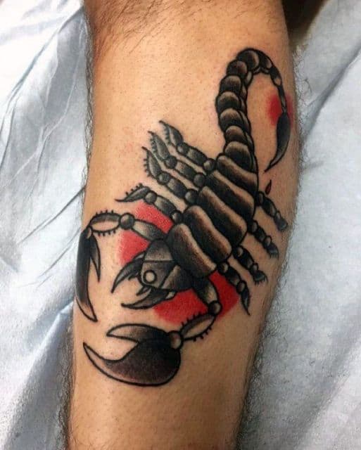 Tatuagem de escorpião feita na perna. Ele é inteiro pintado em tons de preto e há alguns focos de cor vermelha ao fundo que simulam o sol.