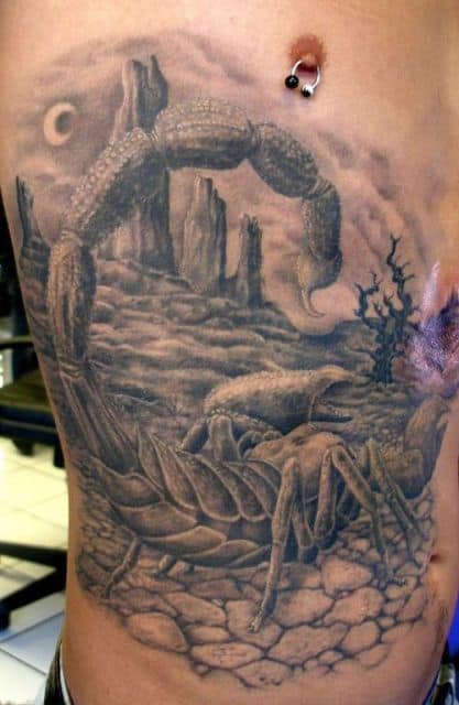 Tatuagem grande na costela de um escorpião andando em um chão rachado com uma paisagem desértica ao fundo. 