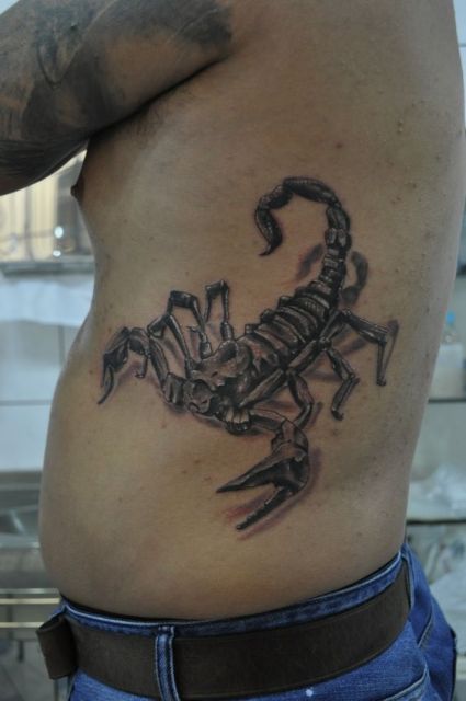 Tatuagem de um escorpião na costela sombreada que também pega parte das costas. 