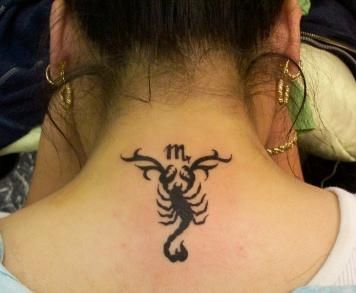 Tatuagem de escorpião na parte superior das costas, próxima ao pescoço, feita no estilo tribal acompanhada da letra M. 