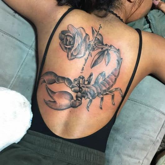 Tatuagem grande de escorpião feita nas costas com uma rosa na ponta de seu ferrão. 