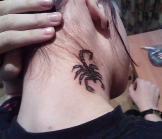 Tatuagem de escorpião simples feita entre a parte de trás e lateral do pescoço vista enquanto a dona da tatto segura o cabelo para torná-la visível. 