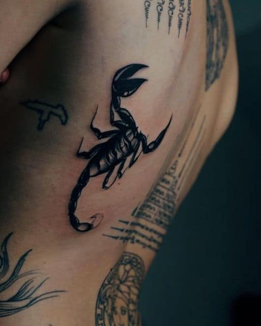 Tatuagem de escorpião feita na lateral das costas próxima de muitas outras tatuagens.