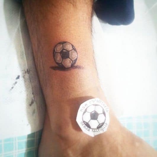 Tatuagem discreta de uma bola de futebol sem maiores detalhes.