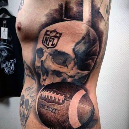 Tatuagem na costela de um crânio com o símbolo da NFL em sua testa e uma bola logo abaixo. 