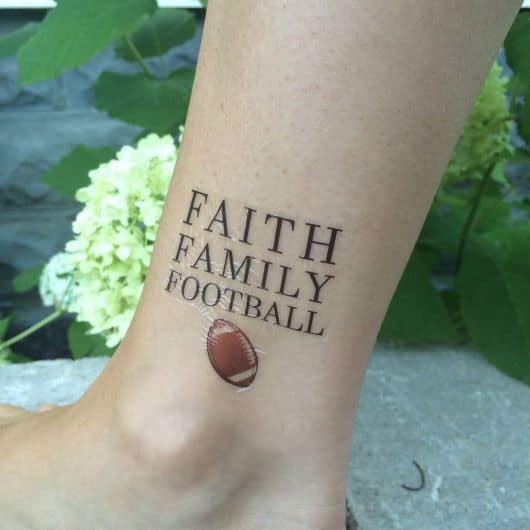 Tatuagem com os dizeres "Faith, Family, Football" e uma bola de futebol americano logo abaixo.
