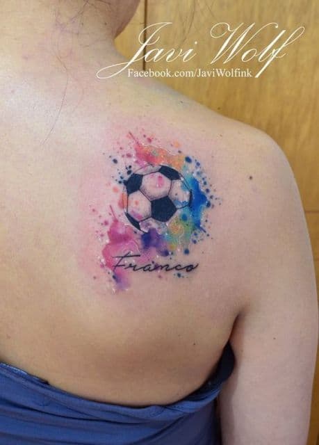 Tatuagem de uma bola de futebol nas costas colorida com tons de aquarela e a palavra "Franco" abaixo dela. 