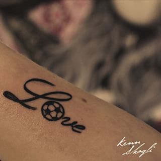 Tatuagem escrita "Love" com uma bola de futebol formando a letra "O". 
