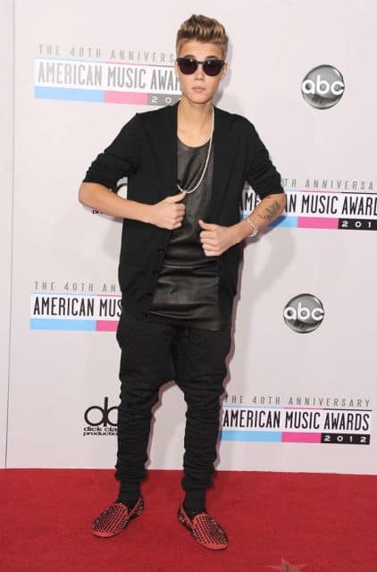 Justin Bieber durante uma premiação vestindo um blazer, camiseta long fit simples, óculos escuros e uma calça swag bem larga. 