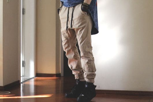 Foto das pernas de um homem vestindo uma calça swag saruel com caimento baixo e apertada na parte de baixo das pernas. 