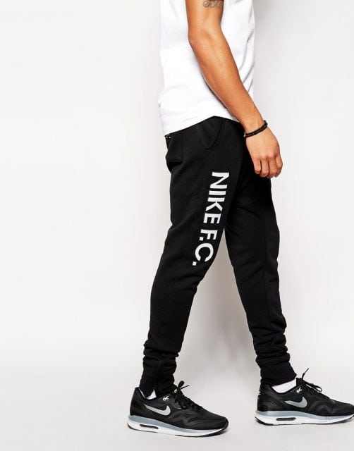 Foto das pernas de um homem de perfil enquanto caminha. Ele veste uma calça swag simples com as palavras Nike F.C em uma das laterais. 