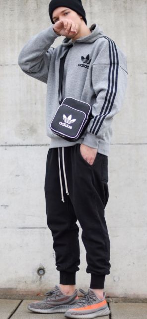 Homem de gorro vestindo um moletom simples com logo da adidas, bolsa lateral da adidas e uma calça jogger de moletom preta. 