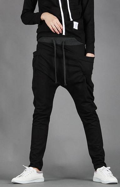 Foto das pernas de um homem com uma das mãos no bolso. Ele veste uma calça jogger preta simples de moletom com caimento baixo. 