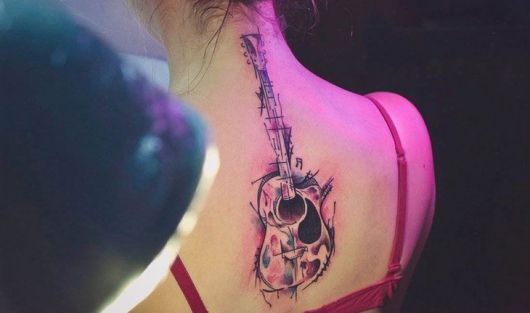 Tatuagem de um violão no centro das costas de uma mulher indo até o pescoço. A tatuagem é feita a partir de aquarela. 