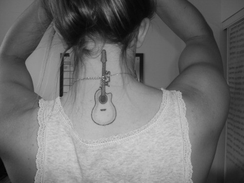 Tatuagem simples de um violão na parte superior das costas de uma mulher que vai até o pescoço. 