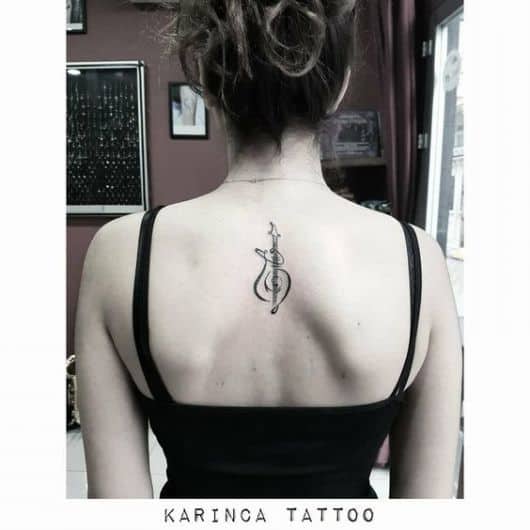Tatuagem do braço de um violão com seu corpo feito a partir de formas sinuosas no centro das costas de uma mulher. 