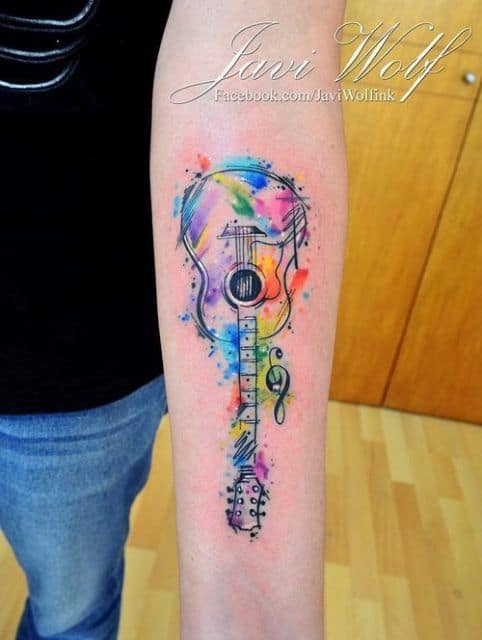 Tatuagem de um violão no antebraço pintado com muitas cores de aquarela. 