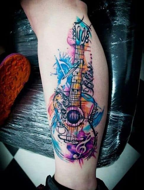 Tatuagem de uma guitarra na perna com muitas cores de aquarela e detalhes abstratos ao seu redor. 