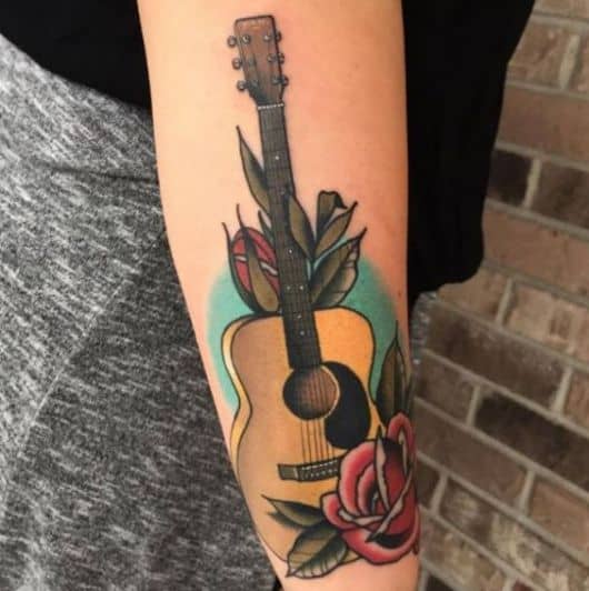 Tatuagem simples de um violão tradicional colorido e flores ao seu redor. 