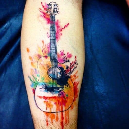 Tatuagem simples de um violão colorido com aquarela que simula uma pintura devido às cores jogadas randomicamente. 