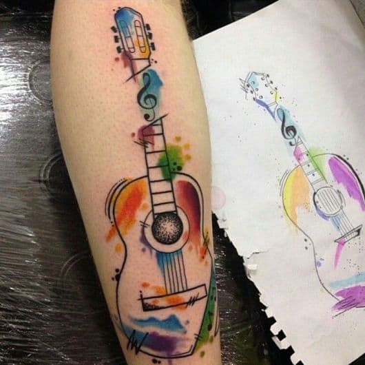 Tatuagem de um violão tradicional pintado com aquarela e uma nota musical que divide seu braço em dois. 