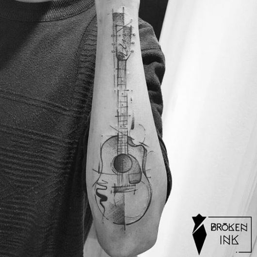 Tatuagem de violão na parte externa do antebraço. A forma como ele é desenhado lembra um esboço. Há diversas linhas e formas ao redor do violão. 