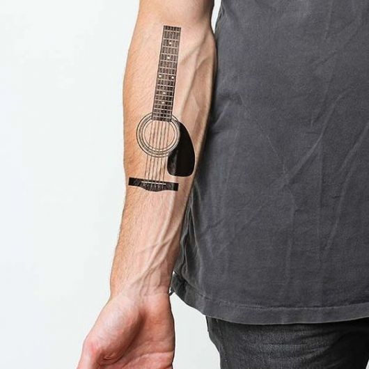 Tatuagem no antebraço de um homem com o desenho de um rastilho, boca, cordas e braço de um violão. Tudo sem contorno. 
