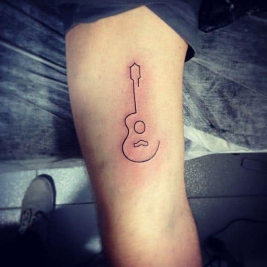 Tatuagem minimalista com o contorno de um violão sem maiores detalhes. 