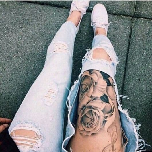 Menina com jeans destroyed e tatuagem de flor na coxa.