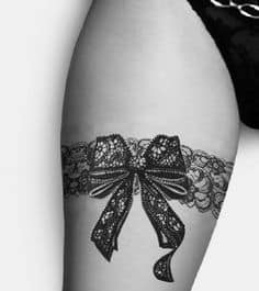 Tatuagem feminina na coxa de cinta liga, com laço.