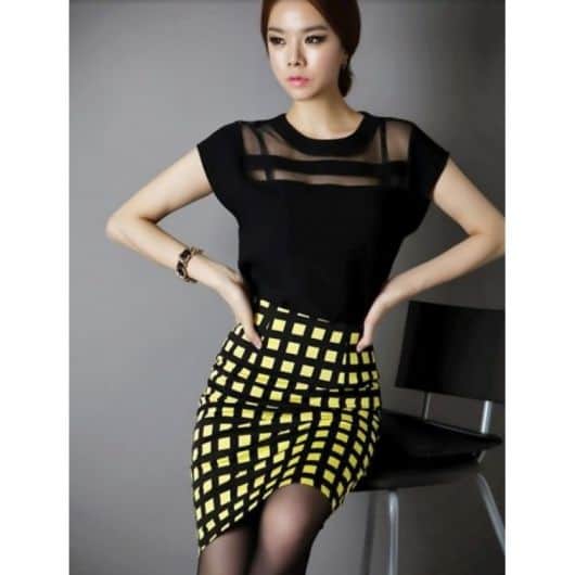 Modelo usa saia estampada nas cores amarelo, preto e blusa preta com detalhes de tule transparente.