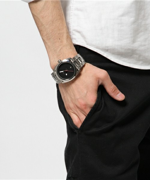 Foto da mão de um homem no bolso com foco no relógio, prata e com detalhes internos, apenas os ponteiros. 