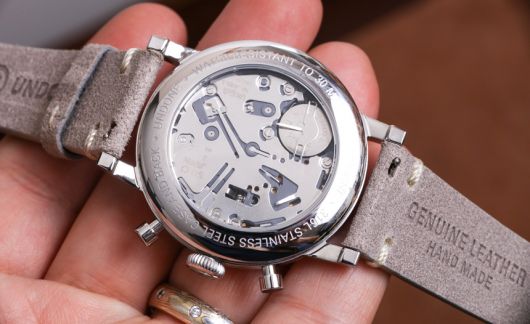 Foto de um relógio na palma da mão de uma pessoa. O aro e interior do relógio contam com diversos detalhes e são feitos em prata, enquanto as pulseiras são feitas de couro. 