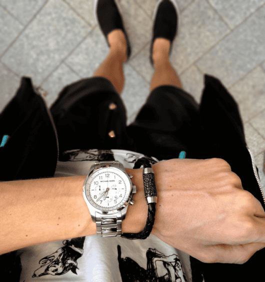 Foto do pulso de um homem que usa um relógio prata arredondado acompanhado de uma pulseira. 