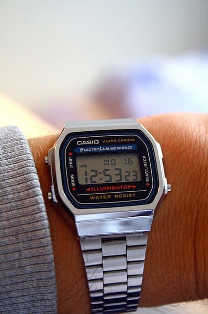 Foto com foco em um relógio no pulso de um homem. O relógio é da marca Casio e tem formato quadrangular, com marcador de horas em numeral. 
