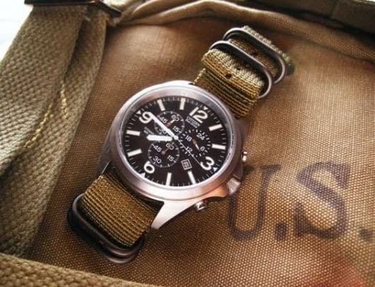 Foto de relógio acima de uma bolsa. Além de marcar as horas, ele conta com funcionalidades e ainda tem uma pulseira forte com diversos prendedores. 