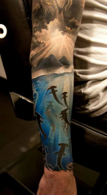 Tatuagem fechando o antebraço com o fundo do mar habito por muitos tubarões martelo nadando em direção à superfície. 